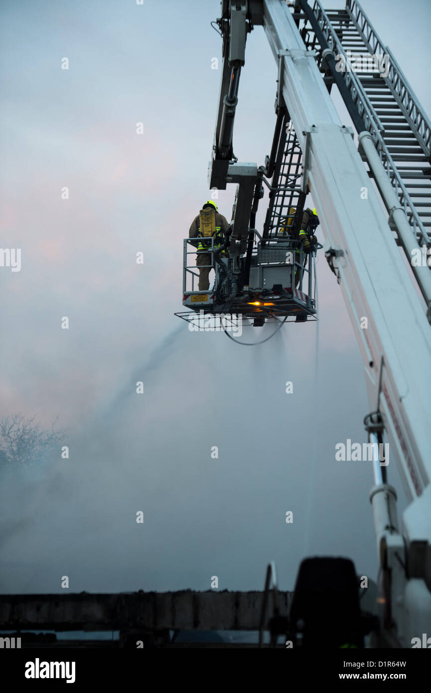 Laindon, Basildon, Essex. Quattro negozi sono stati rasi al suolo dopo un incendio appiccato in un cinese take-away in parata noto come il Triangolo negozi. Si ritiene che l incendio è scoppiato in un aeratore e diffondersi a tutta la sfilata di distruggere altre tre imprese. Gli altri negozi erano un parrucchiere, un ufficio postale e un negozio di generi alimentari. Non è noto per aver causato danni. Due vigili del fuoco su di una piattaforma aerea la spruzzatura del tetto. Foto Stock