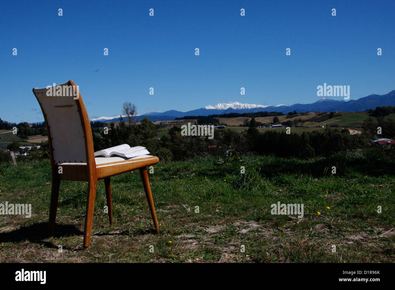 Una sedia con un libro rivolto verso le montagne innevate di Kahurangi National Park. Foto Stock