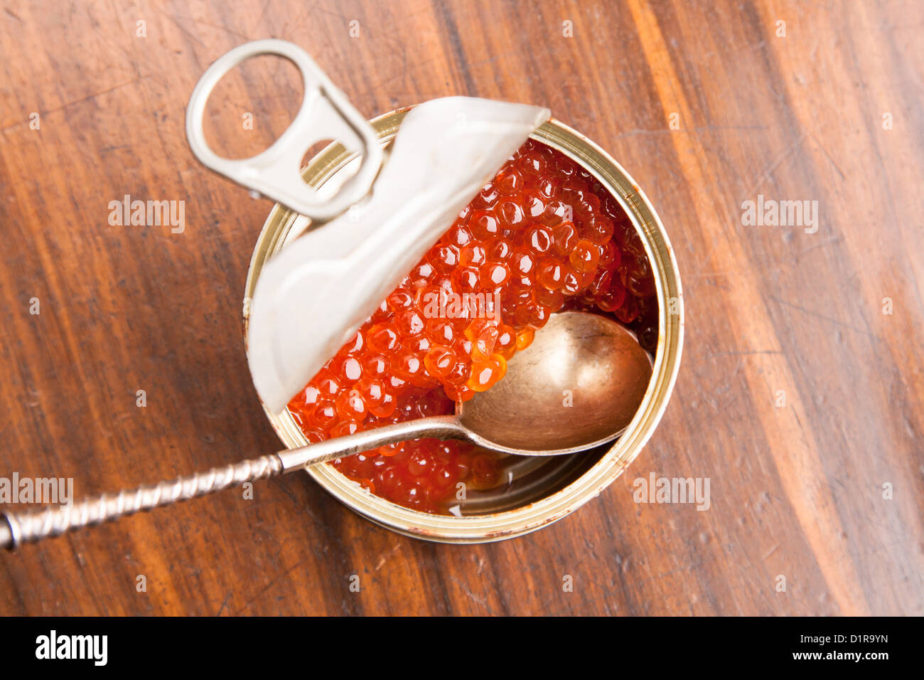 Caviale rosso in banca con il cucchiaio su uno sfondo di legno Foto Stock