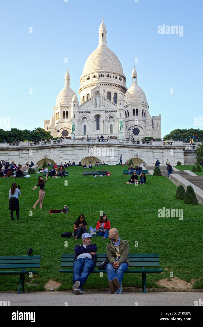 Le persone si radunano e socializzare nella luce della sera intorno al Sacre Coeur basilica nella zona di Montmartre di Parigi, Francia Foto Stock