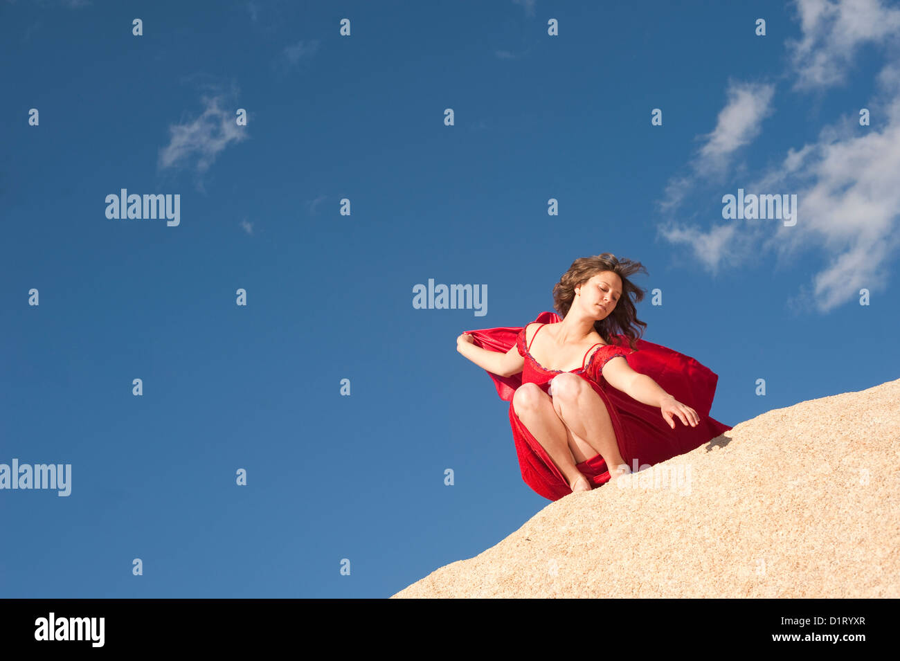 La donna in un abito rosso alta su una pietra paesaggio con big sky. Foto Stock