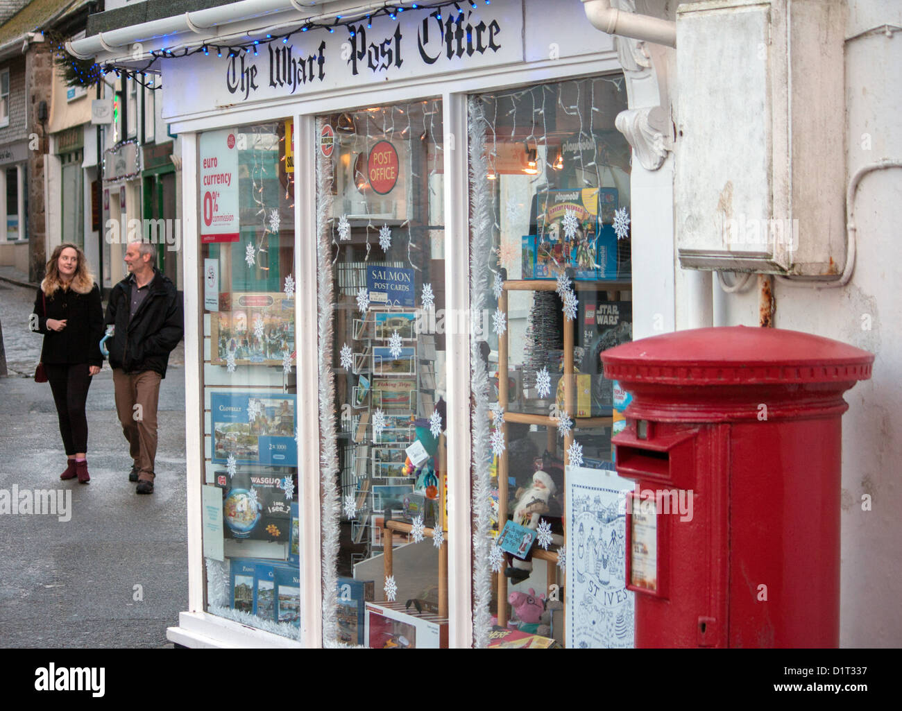 Un pilastro rosso box esterno il Wharf Post Office, St. Ives, con una giovane coppia passeggiando a. Foto Stock