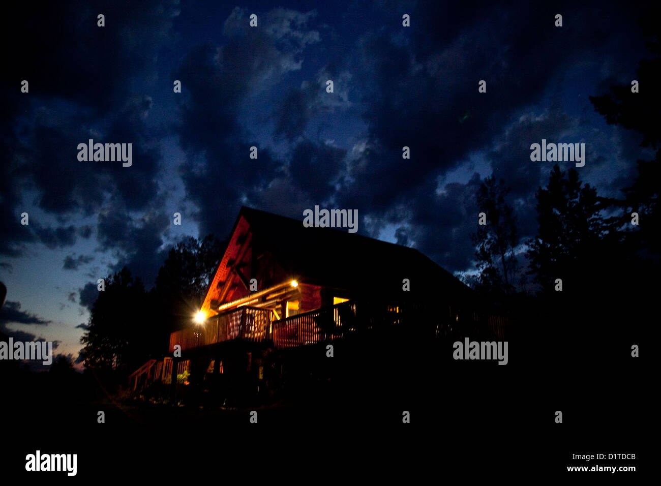 Una illuminata vivamente cottage home è impostata contro un blu scuro offuscato sunsetting sky. Foto Stock