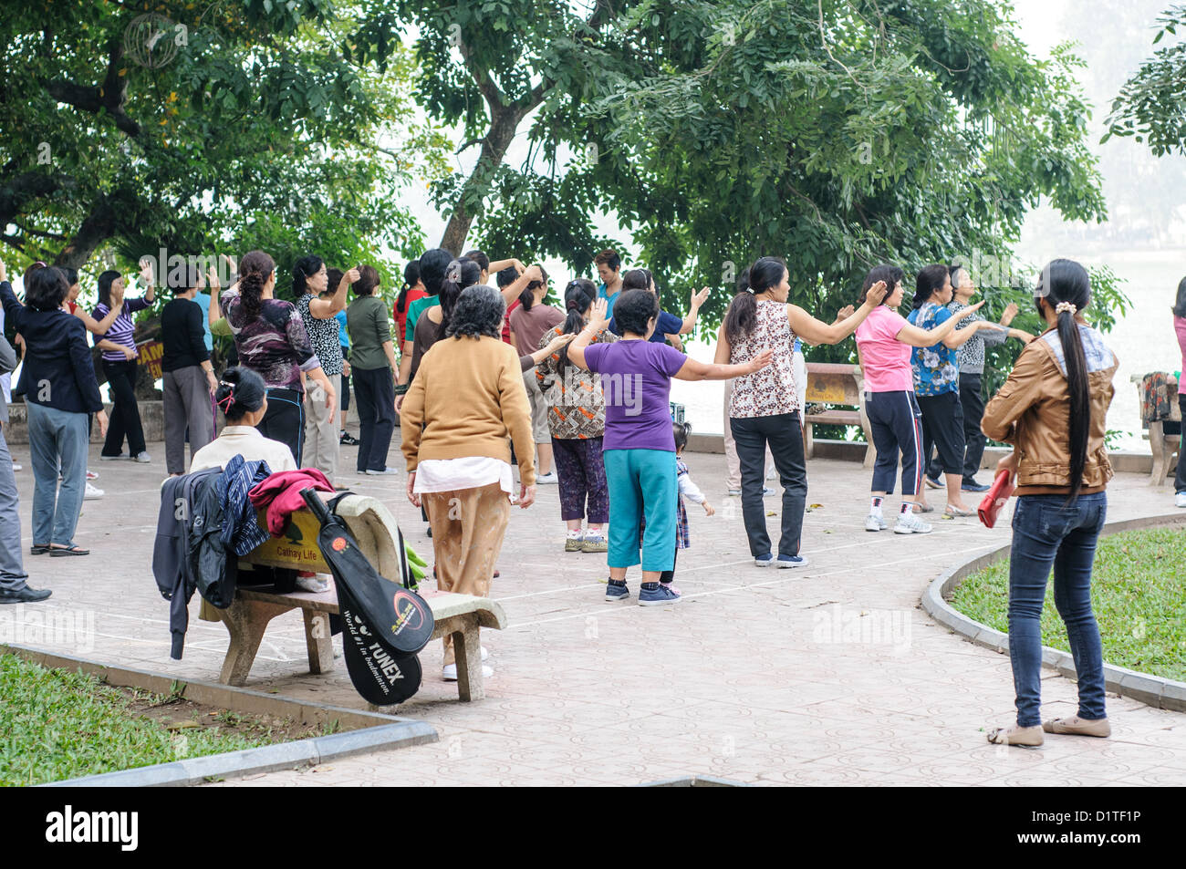 Esercizio di Tai chi presso il lago Hoan Kiem Hanoi Vietnam // HANOI, Vietnam - le donne locali praticano Tai chi durante la loro routine mattutina lungo le rive del lago Hoan Kiem nel centro di Hanoi. L'incontro quotidiano rappresenta un aspetto tradizionale della cultura urbana vietnamita, combinando l'esercizio fisico con l'interazione sociale. Il lago è un luogo popolare per le attività della comunità nel cuore del centro storico della città. Foto Stock