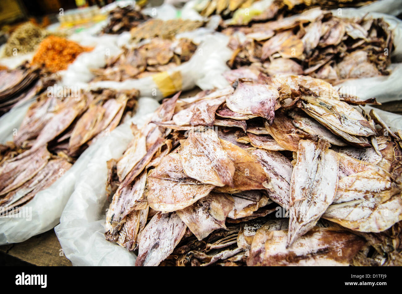 Pesce secco al mercato mattutino di Luang Prabang Laos // LUANG PRABANG, Laos - Un venditore propone pesce secco e salato, tra cui calamari, gamberi e pesce al mercato mattutino. Questi prodotti conservati servono come ingredienti essenziali nella cucina tradizionale del Laos, fornendo fonti proteiche che possono essere conservate senza refrigerazione nel clima tropicale. Le tecniche di conservazione dell’essiccazione e della salatura consentono lo stoccaggio e il trasporto a lungo termine dei prodotti ittici dalle zone costiere ai mercati interni del Laos. Il mercato mattutino di Luang Prabang funge da centro centrale per il commercio locale, dove Foto Stock