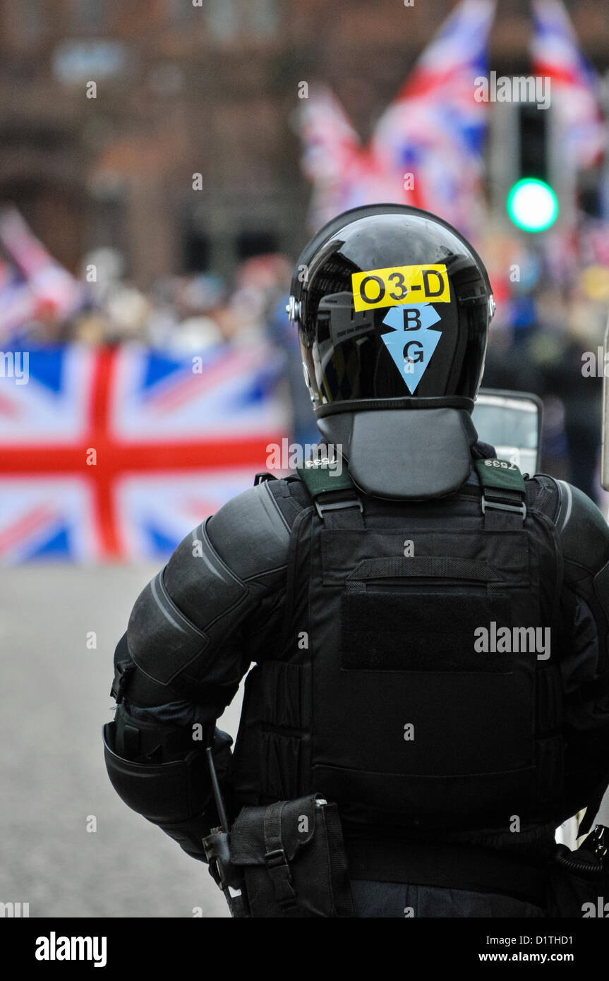 Dal 5 gennaio 2013. Belfast, Irlanda del Nord - un PSNI Officer dal Supporto tattico di gruppo (TSG) orologi una folla portando bandiere dell'Unione. Foto Stock