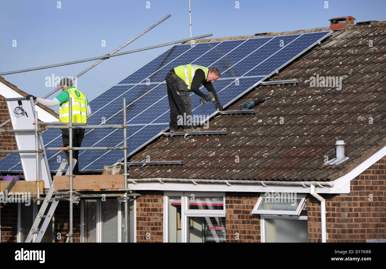 Operai montaggio di pannelli solari per un interno sul tetto della casa di Re bollette energetiche costi prezzi SUN POWER elettricità griglia nazionale britannico di calore Foto Stock