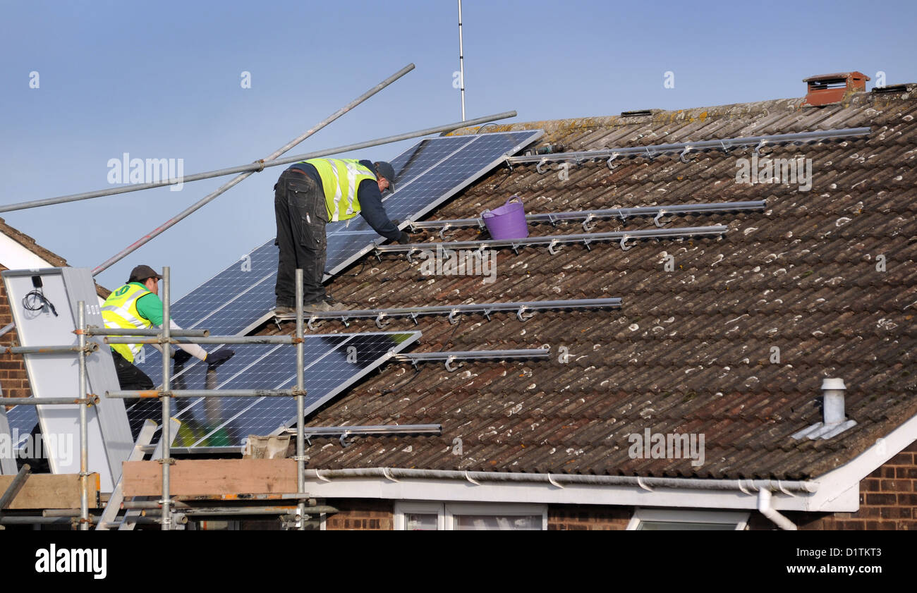 Operai montaggio di pannelli solari per un interno sul tetto della casa di Re bollette energetiche costi prezzi SUN POWER elettricità griglia nazionale britannico di calore Foto Stock