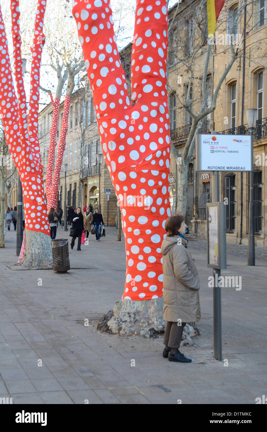 Donna in attesa alla fermata dell'autobus accanto al piano avvolto albero decorato con rosso e bianco Polka Dot Paper da artista giapponese Yayoi Kusama Cours Mirabeau Aix-en-Provence per l'inaugurazione di Marsiglia-Provenza 2013 capitale europea della cultura. Provenza francia Foto Stock