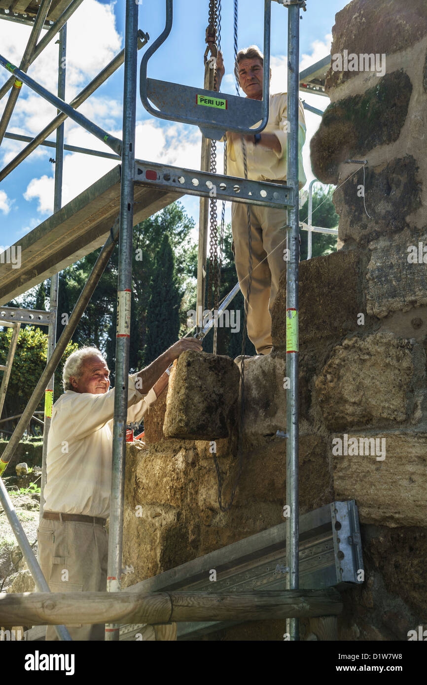 Spagna, Andalusia - Antequera. Operai usare la puleggia e la catena per sollevare Pesanti in muratura la riparazione della Alcazaba gateway (leva). Foto Stock