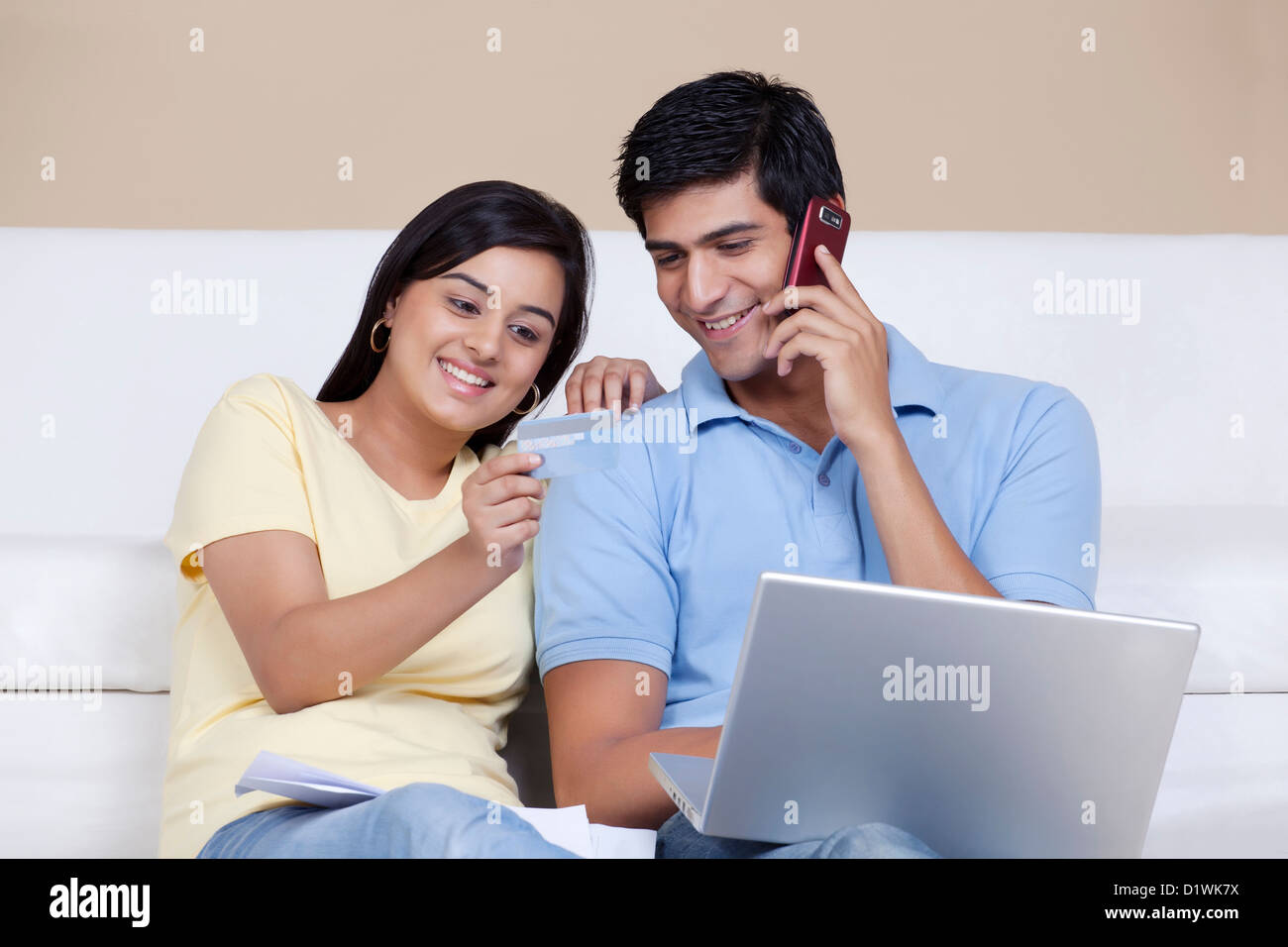 La donna che mostra la carta di credito al uomo mentre parlano al telefono e tramite computer portatile Foto Stock
