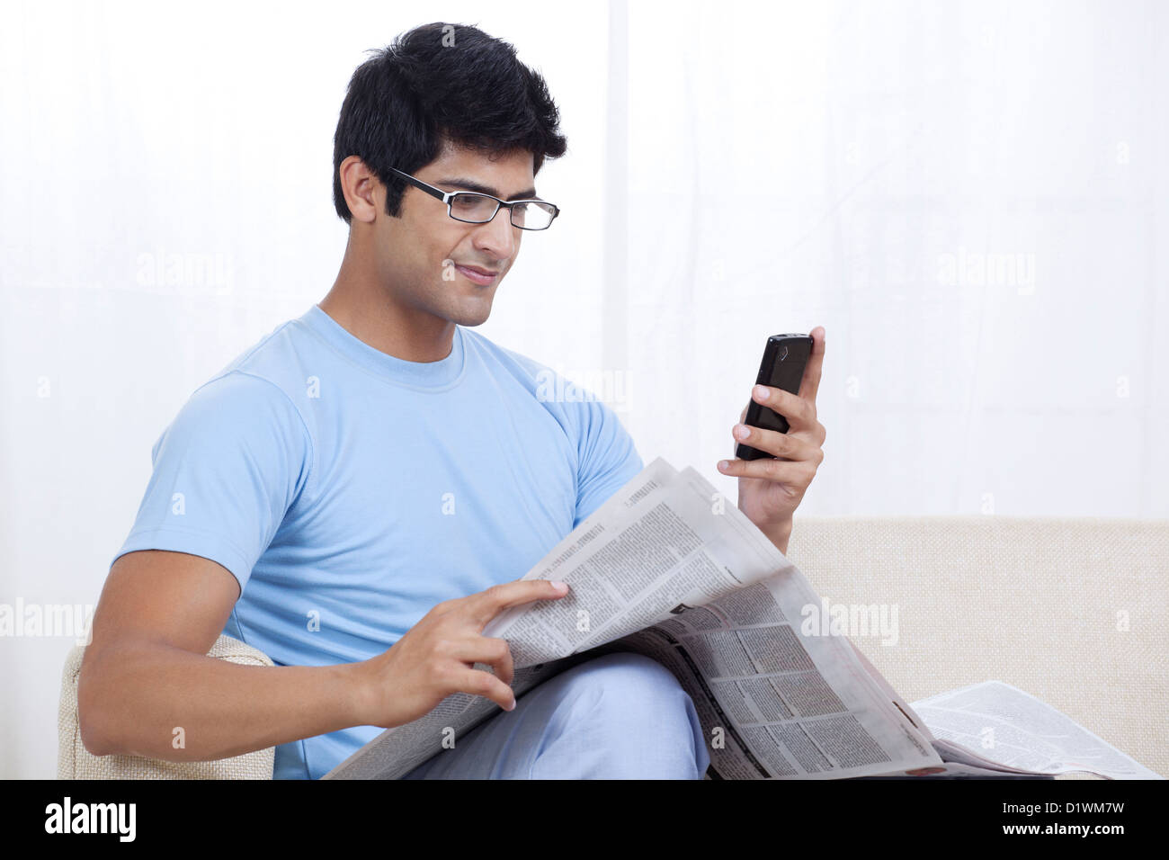 Giovani indiani un uomo guarda il telefono mobile con quotidiano Foto Stock