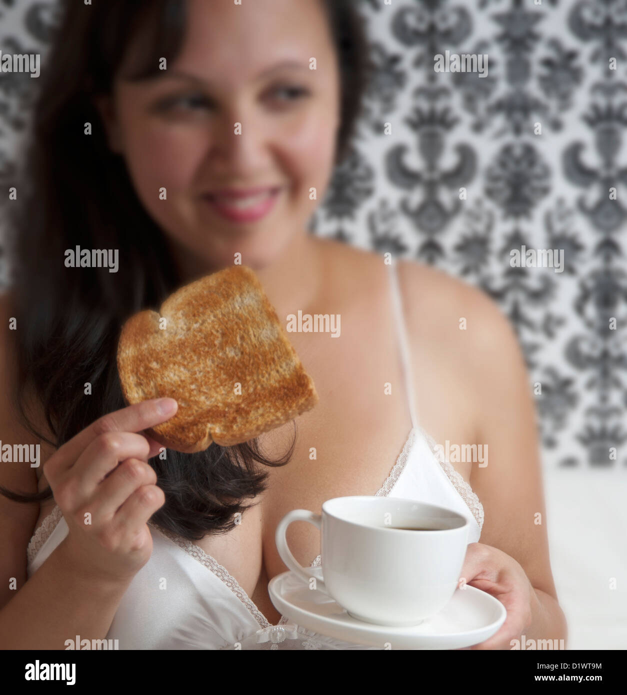 Bella donna seduta nel letto con colazione a base di pane tostato e caffè Foto Stock
