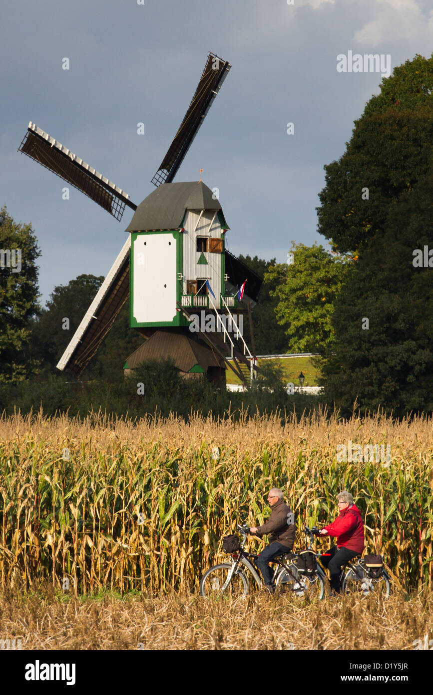 Un mulino a vento nei Paesi Bassi, si vede attraverso i campi con i ciclisti in primo piano Foto Stock