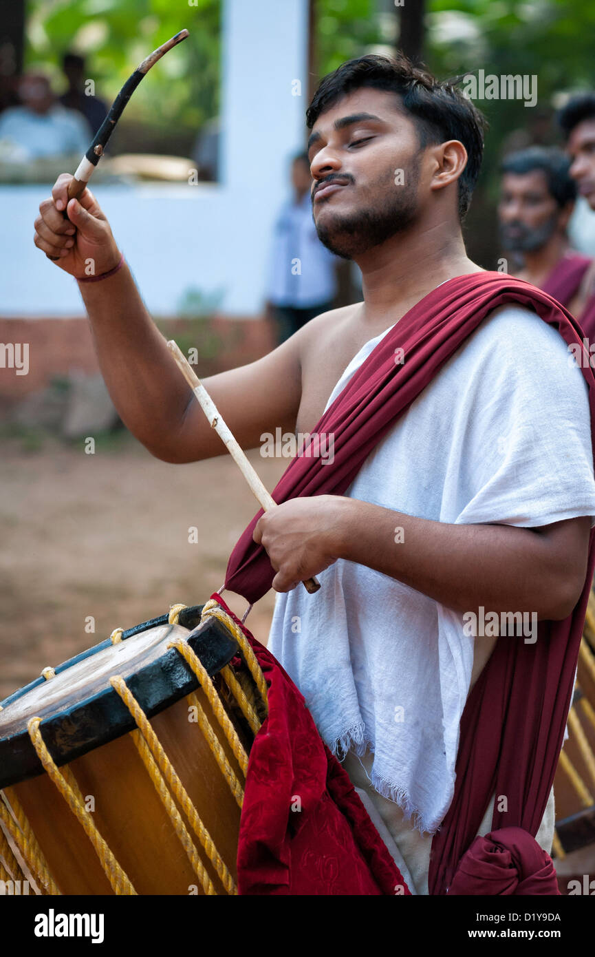 Un tradizionale percussionista batte un ritmo complesso sul suo tamburo durante una performance di Theyyam, una danza religiosa/dramma. Foto Stock