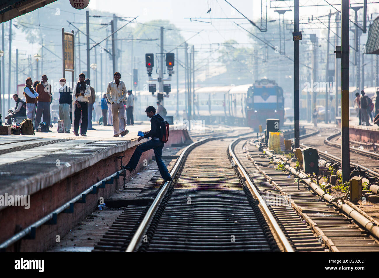 Giovane uomo attraversando le vie di fronte a un treno in arrivo, New Delhi Raliway Station, New Delhi, India Foto Stock