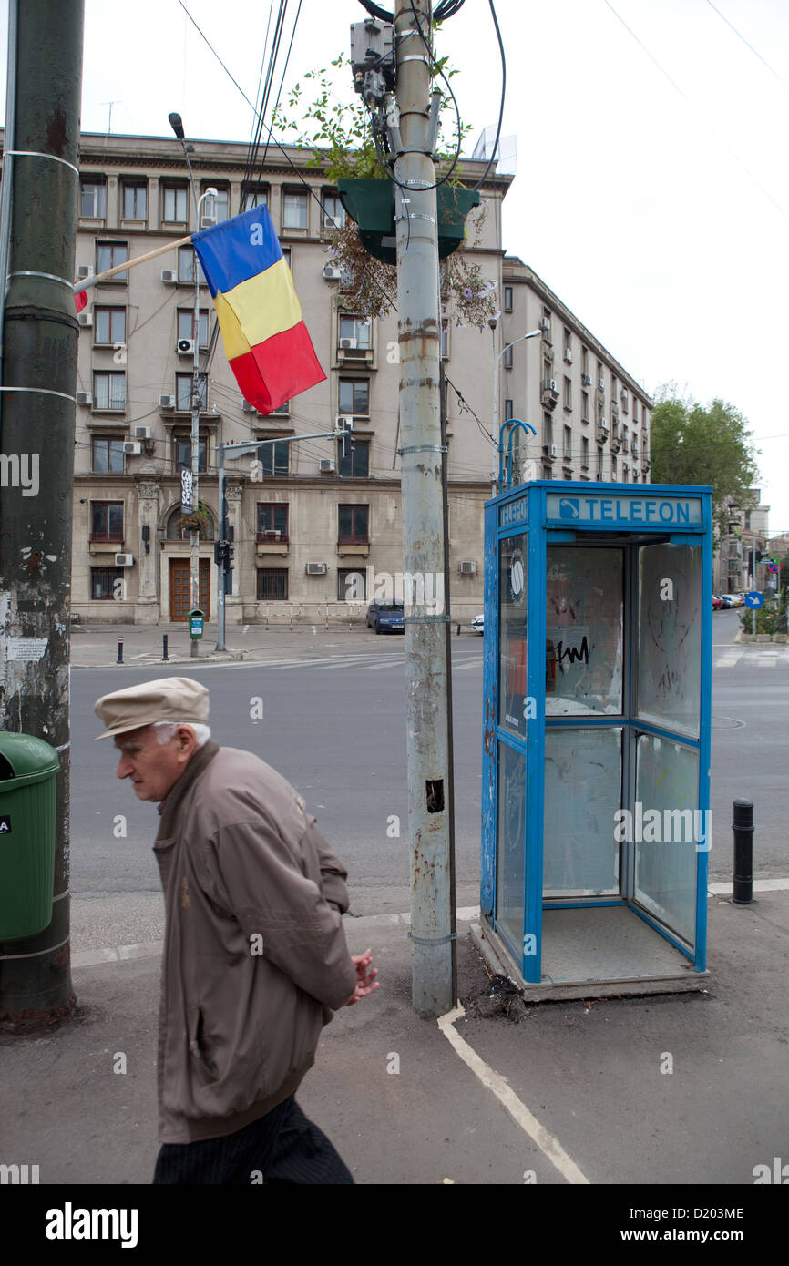 Bucarest, Romania, un vecchio uomo cammina oltre la bandiera rumena e Telefonhaeuschen Foto Stock