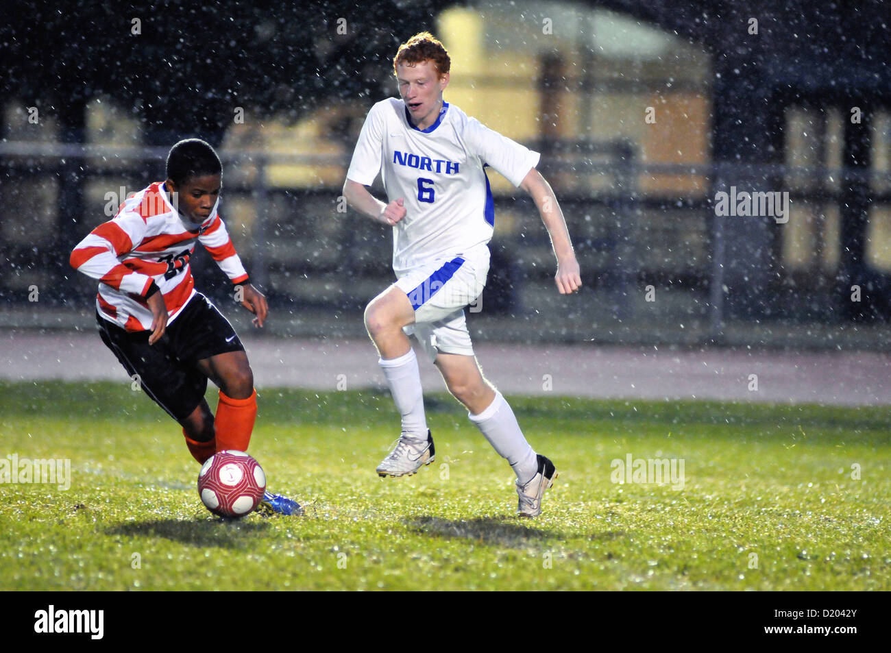 I giocatori di calcio battaglia per il possesso di palla su una molto soggy passo durante una scuola di match. Stati Uniti d'America. Foto Stock