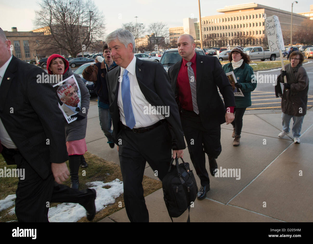 Lansing, Michigan - Michigan governatore Rick Snyder (cravatta blu) arriva al Campidoglio per il giorno di apertura del 2013 Michigan sessione legislativa. Elementi di raccordo picketed il captiol, protestando un "diritto al lavoro" legge che Snyder firmato nei giorni di chiusura del 2012 sessione legislativa. Foto Stock