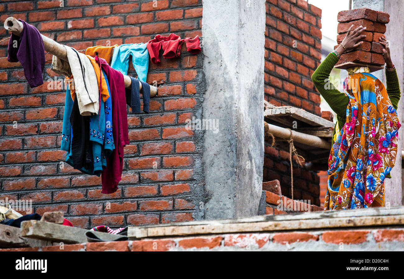 Donna che la porta in mattoni a un sito construciton nella colonia di difesa, Delhi, India Foto Stock