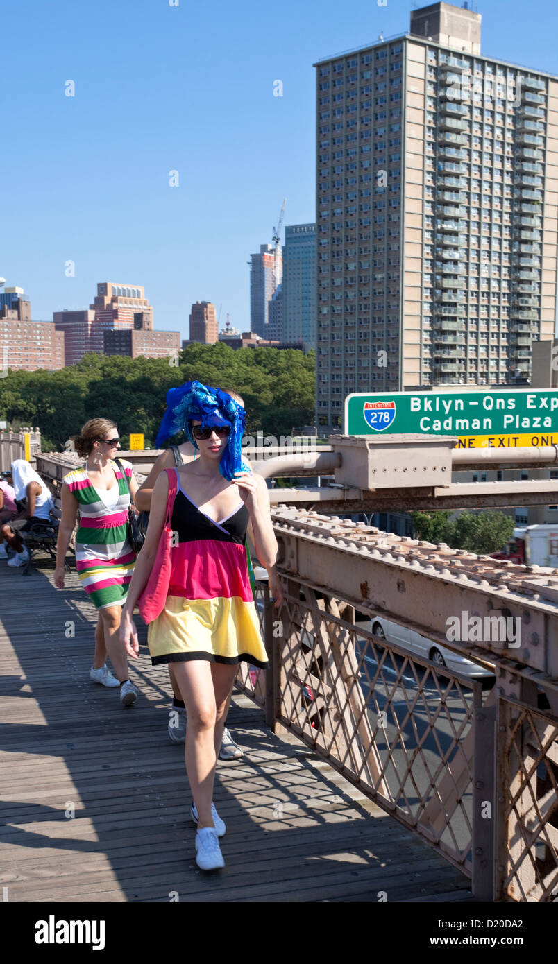 Un quartiere alla moda di giovane donna che indossa un vestito colorato, percorrendo a piedi il Ponte di Brooklyn, New York City, Stati Uniti d'America. Foto Stock