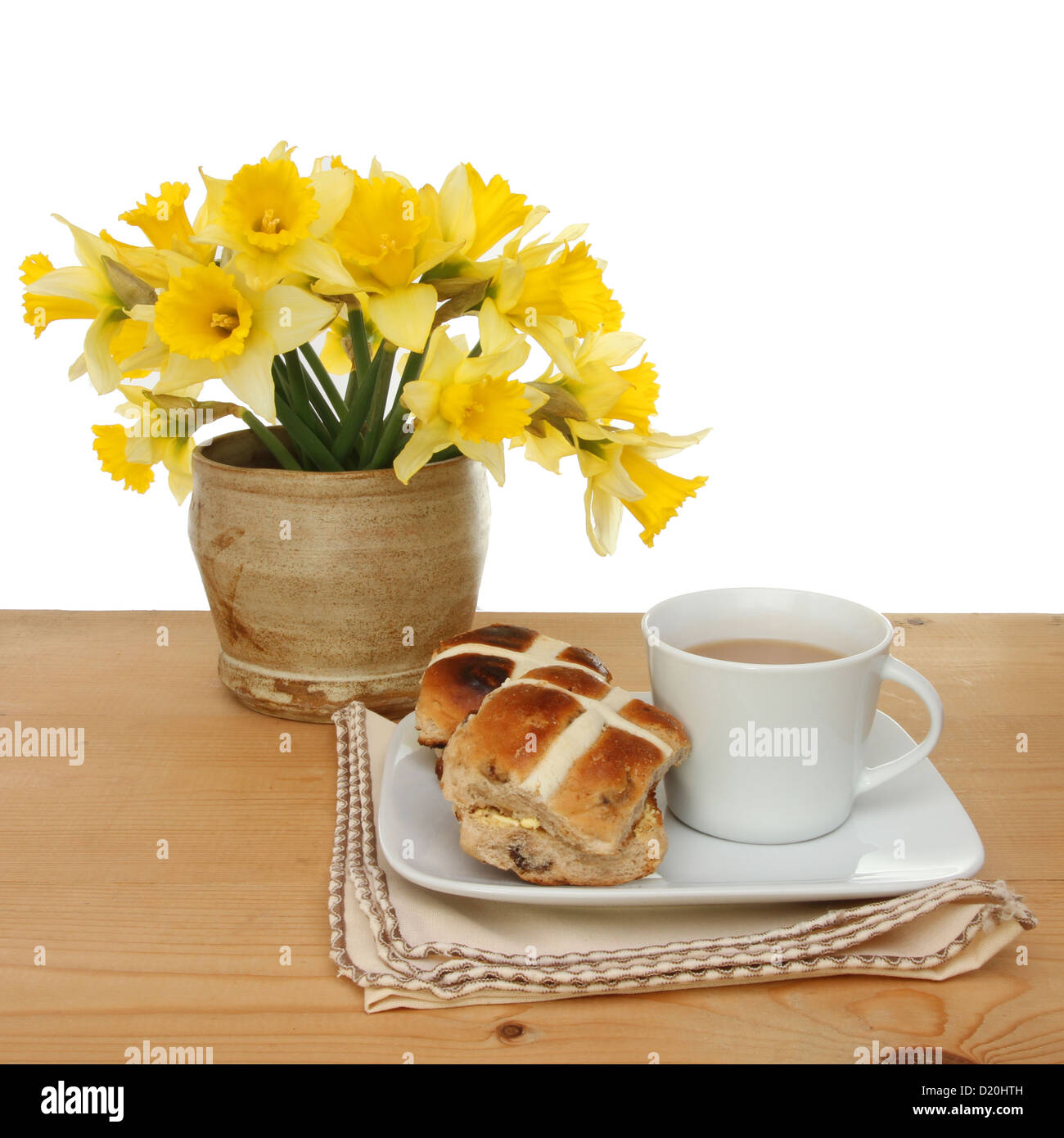 Pasqua tema, hot cross panini e una tazza di tè con daffodil fiori su un tavolo contro uno sfondo bianco Foto Stock