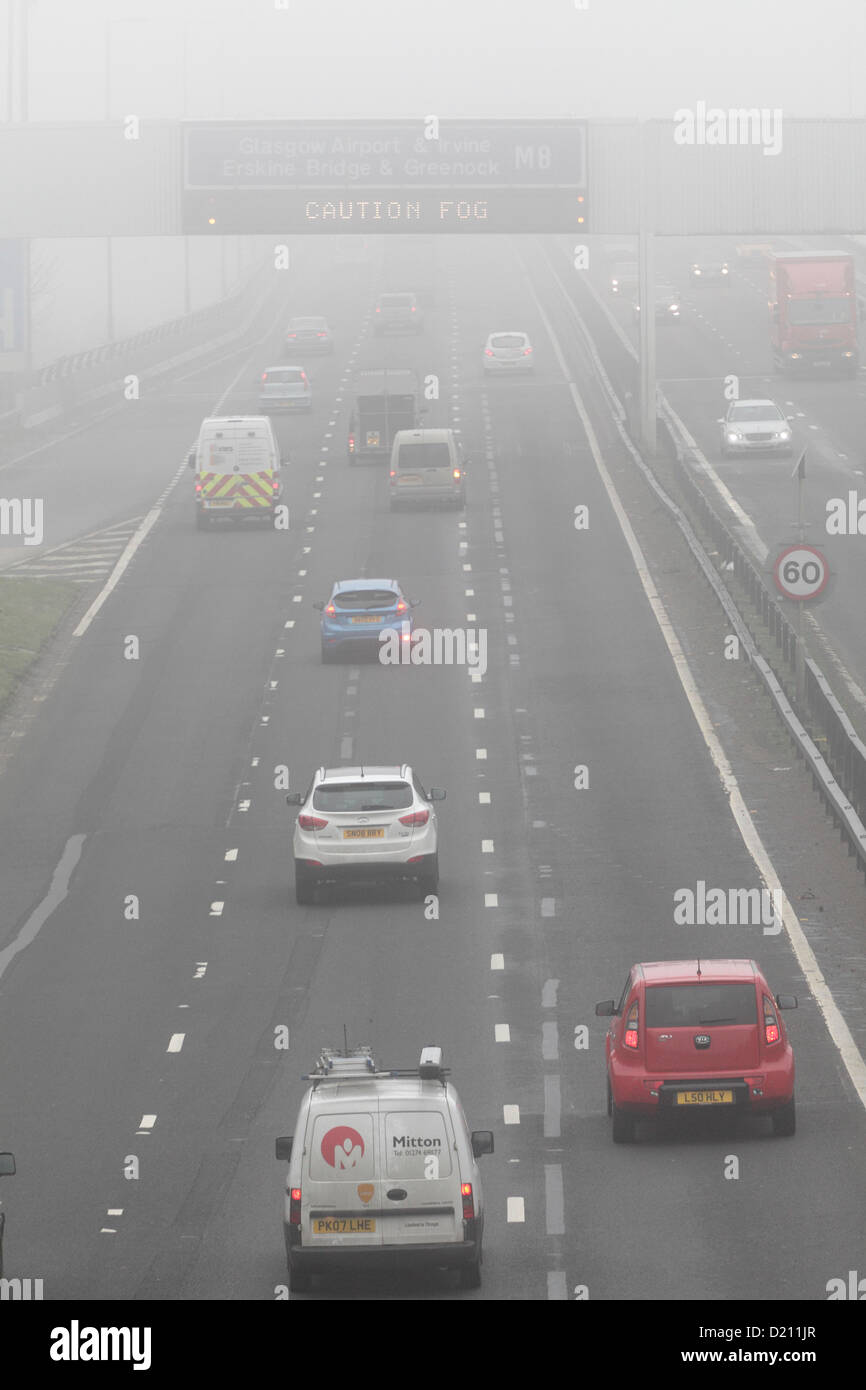 White Cart Viaduct, Arkleston, Renfrewshire, Scozia, Regno Unito, giovedì, 10 gennaio, 2013. Traffico che attraversa la nebbia sull'autostrada M8 con la scritta attenzione nebbia visualizzata su un cartello a LED del gantry Foto Stock