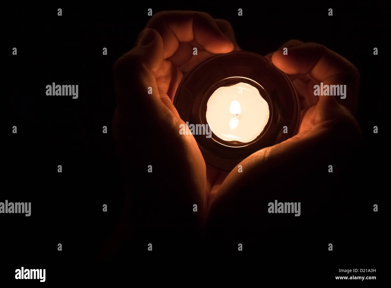 Mani in forma di cuore intorno a una candela accesa. Foto Stock