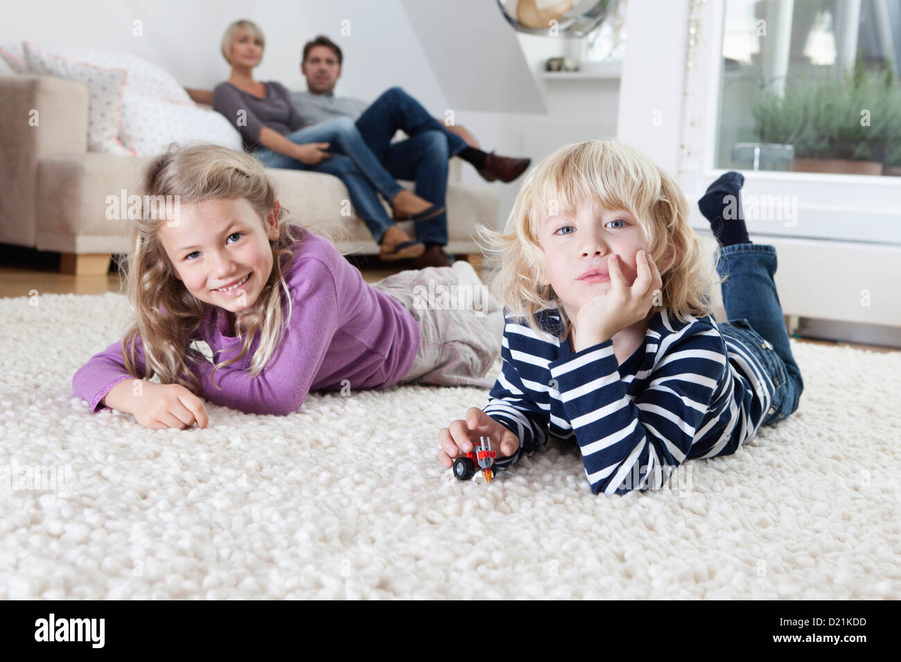 In Germania, in Baviera, Monaco di Baviera, un ragazzo e una ragazza che giace sul pavimento, genitori seduta del divano in background Foto Stock
