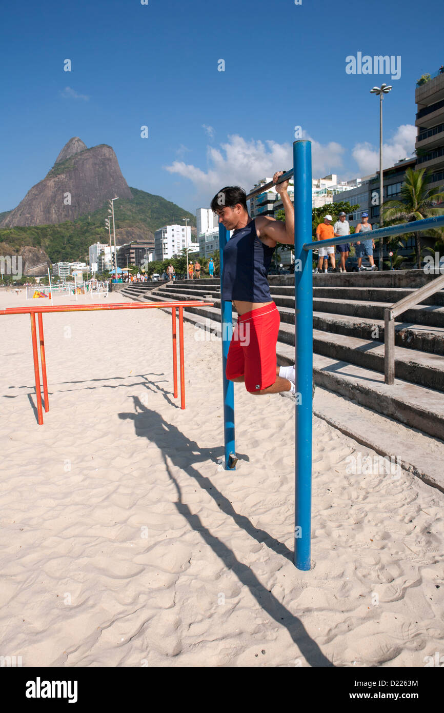 Un uomo che sta facendo il suo mattina pull-up esercizi in palestra a cielo aperto sulla spiaggia di Ipanema Foto Stock
