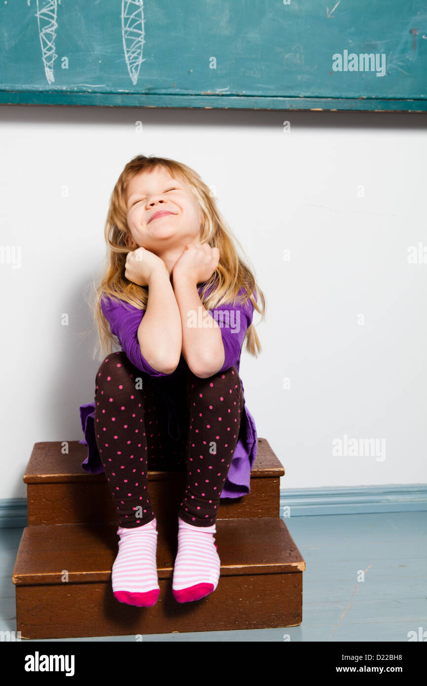 Ritratto in studio di sorridente ragazza seduta di fronte a lavagna in aula con gli occhi chiusi Foto Stock