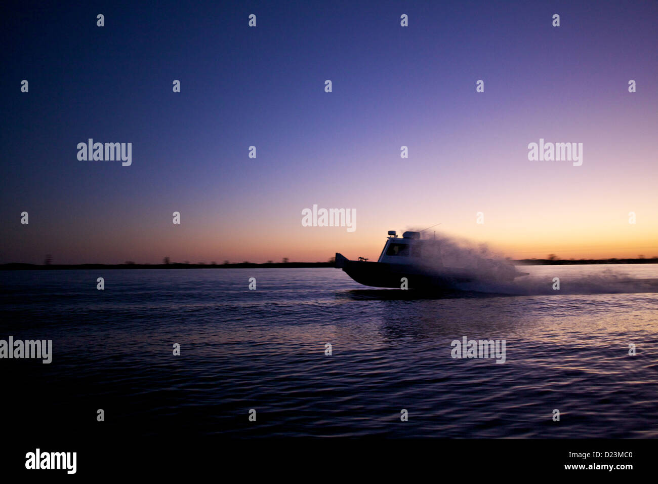 Motoscafo che attraversa le acque del Delta della Louisiana al crepuscolo, con un cielo vibrante e riflessi ondulati catturati in una vista grandangolare Foto Stock