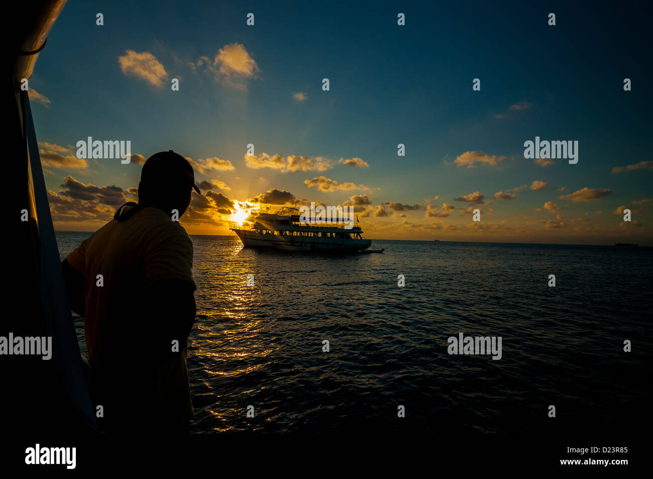 L'uomo a guardare il sole sorgere su una barca in mezzo al mare dei Caraibi Foto Stock
