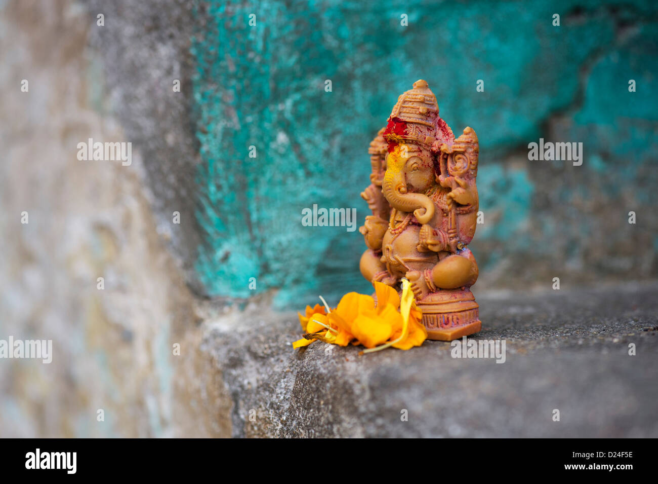 Elefante indù Dio. Signore Ganesha statua e petali di fiori contro la parete colorata. India Foto Stock