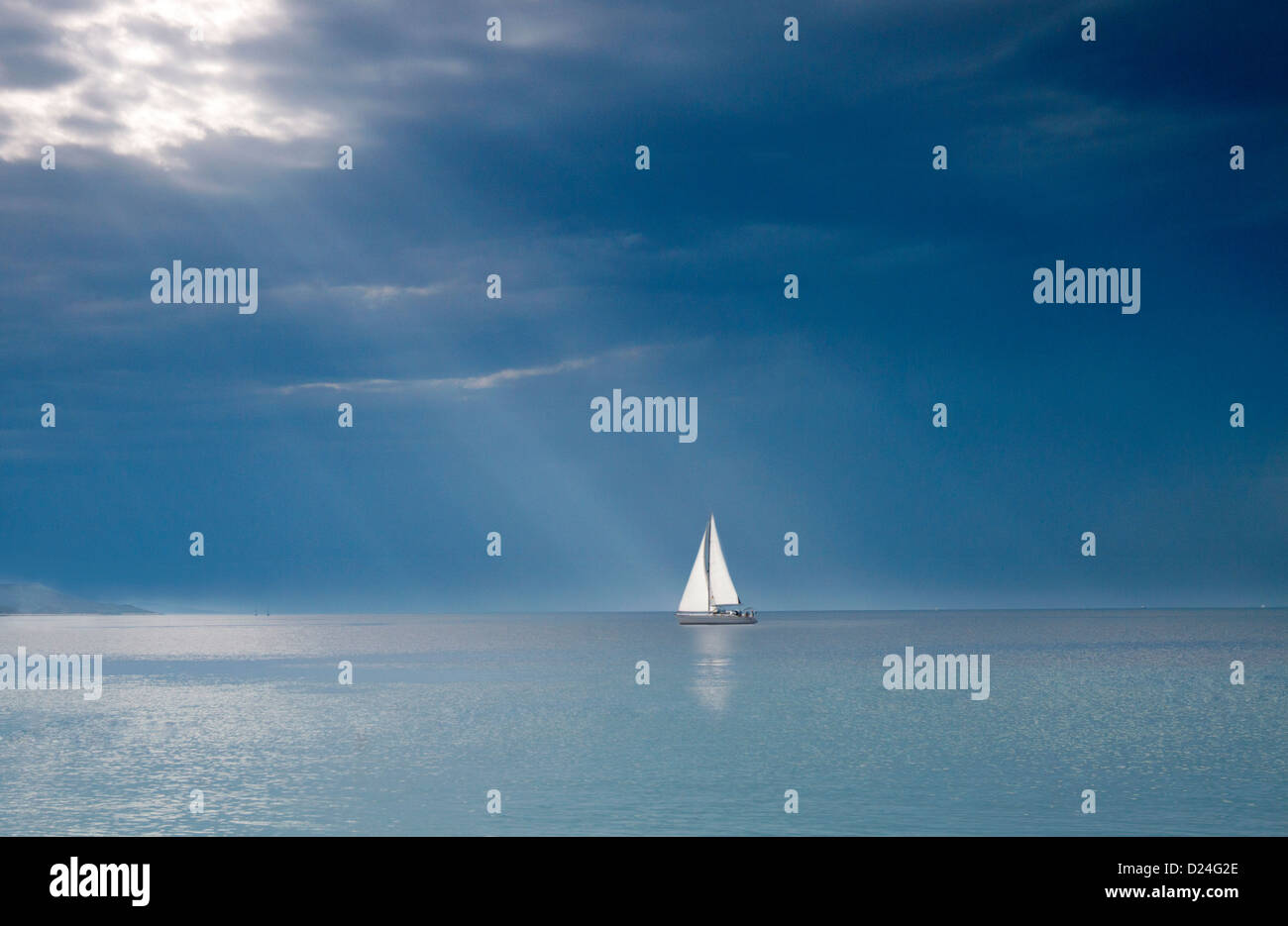 Una imbarcazione a vela vela verso alcuni raggi del sole sull'oceano. Foto Stock