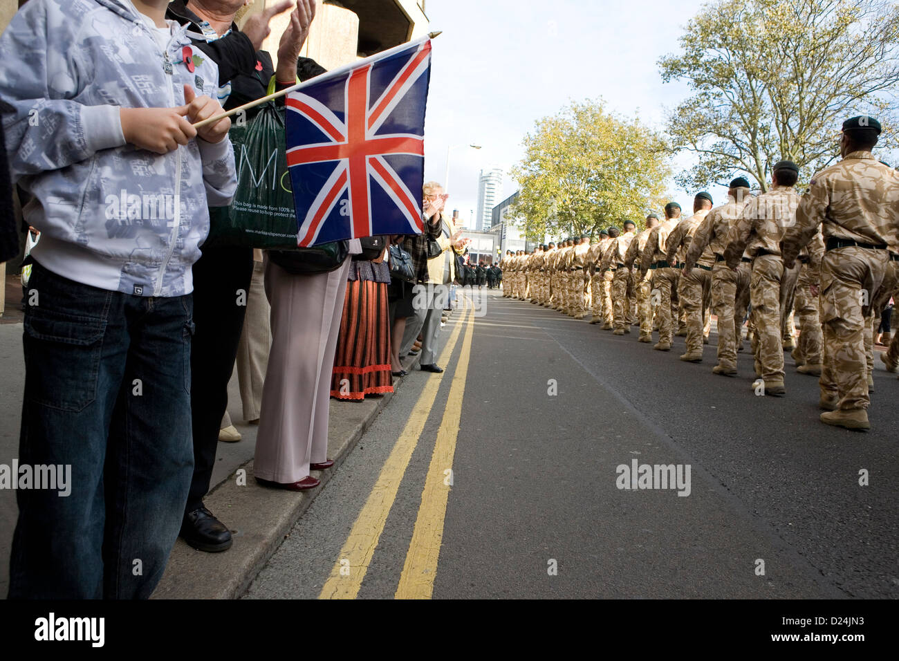 Un giovane ragazzo tenendo un Union Jack flag come soldati britannici marzo passato. Foto Stock