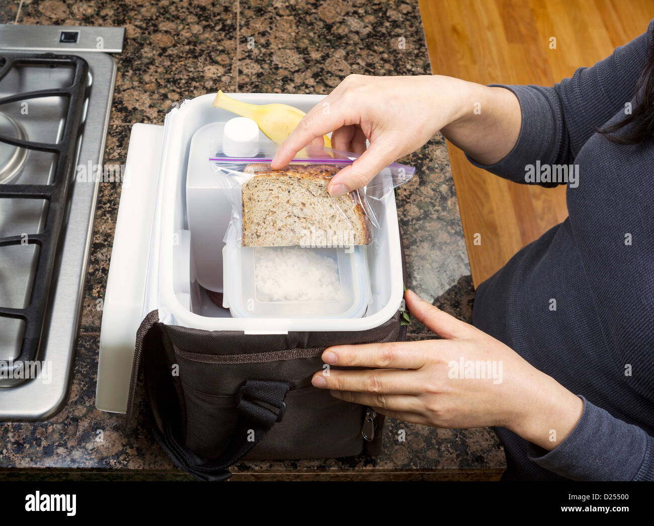 Mani femminili pranzo di imballaggio in borsa per portatile mentre in cucina su pietra bancone accanto alla stufa Foto Stock