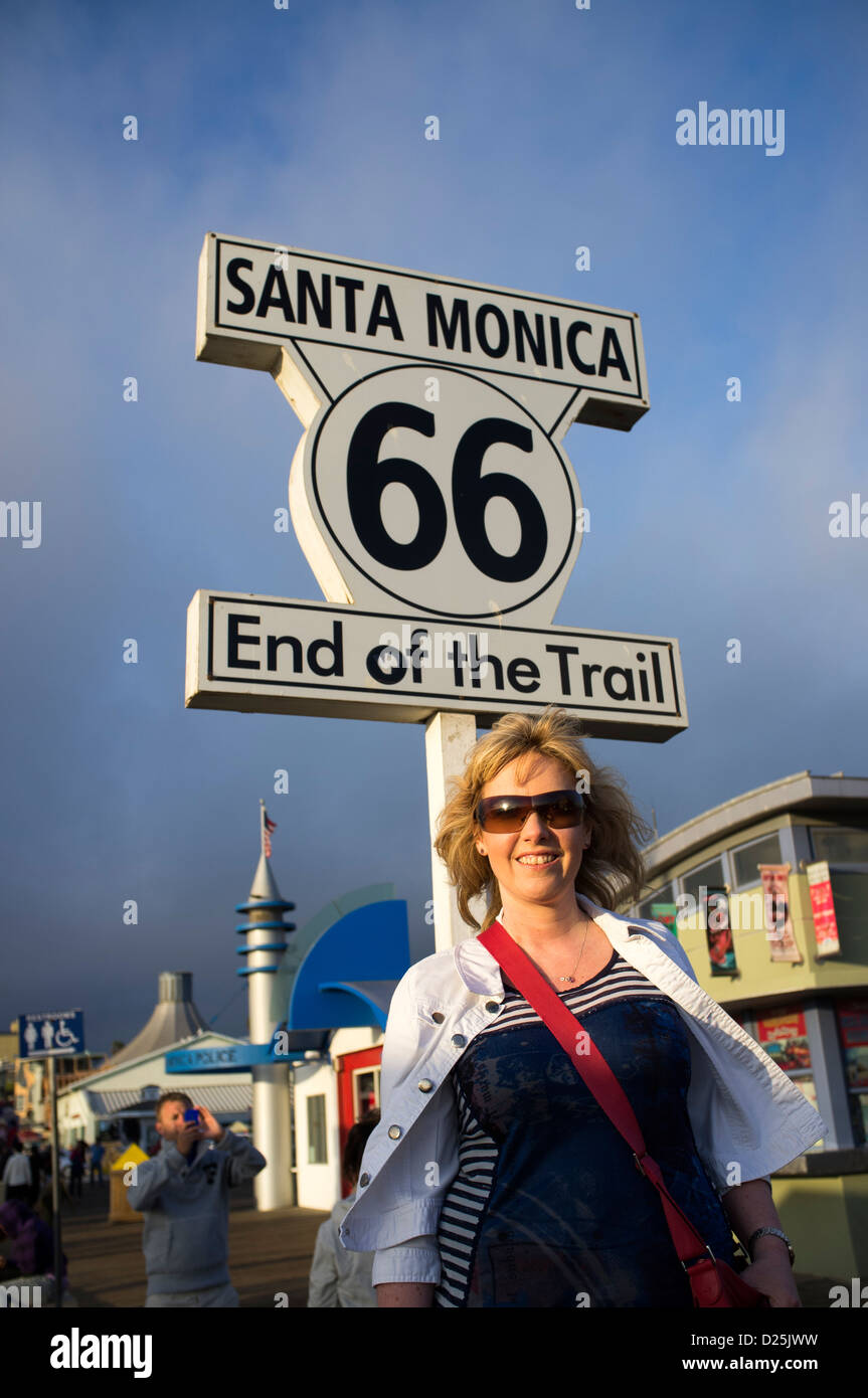 Fine della Route 66 segnavia a Santa Monica Pier con la donna in piedi al di sotto di Foto Stock