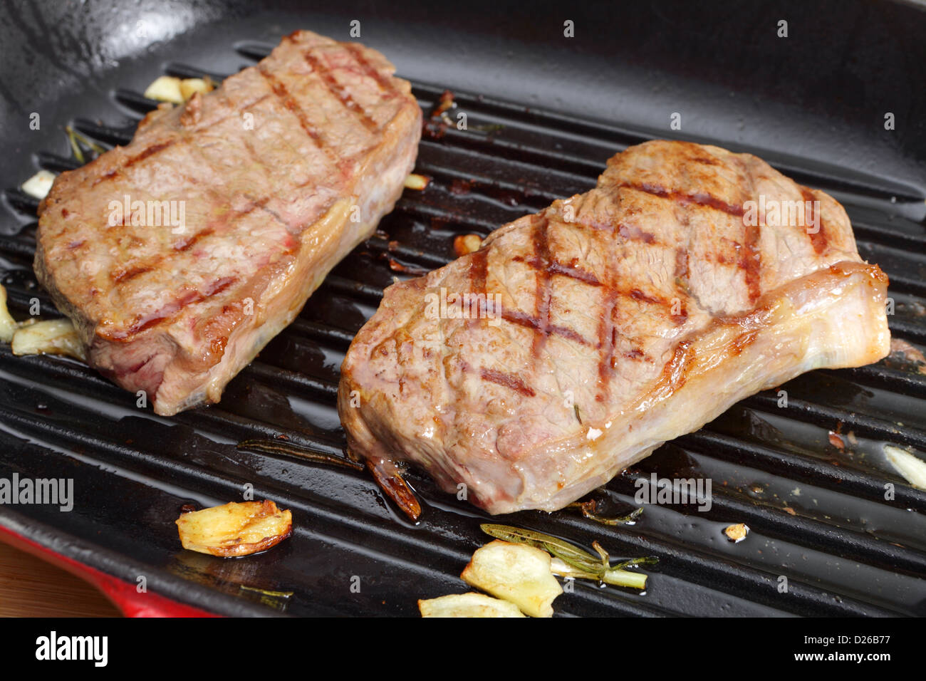 Due controfiletto (o a New York) bistecche grigliare in una padella con aglio e rosmarino Foto Stock