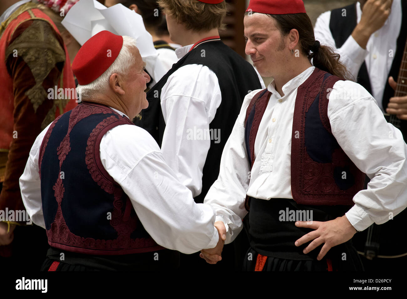 Due elementi maschio del gruppo folk stringono le mani a Cilipi. Foto Stock