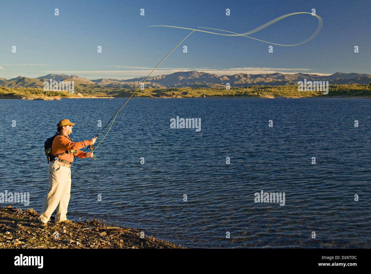 Uomo di Pesca a Mosca Report di Pesca lungo il deserto litorale del Lago di piacevole con le colline pedemontane dell'Bradshaw montagne in distanza. Foto Stock