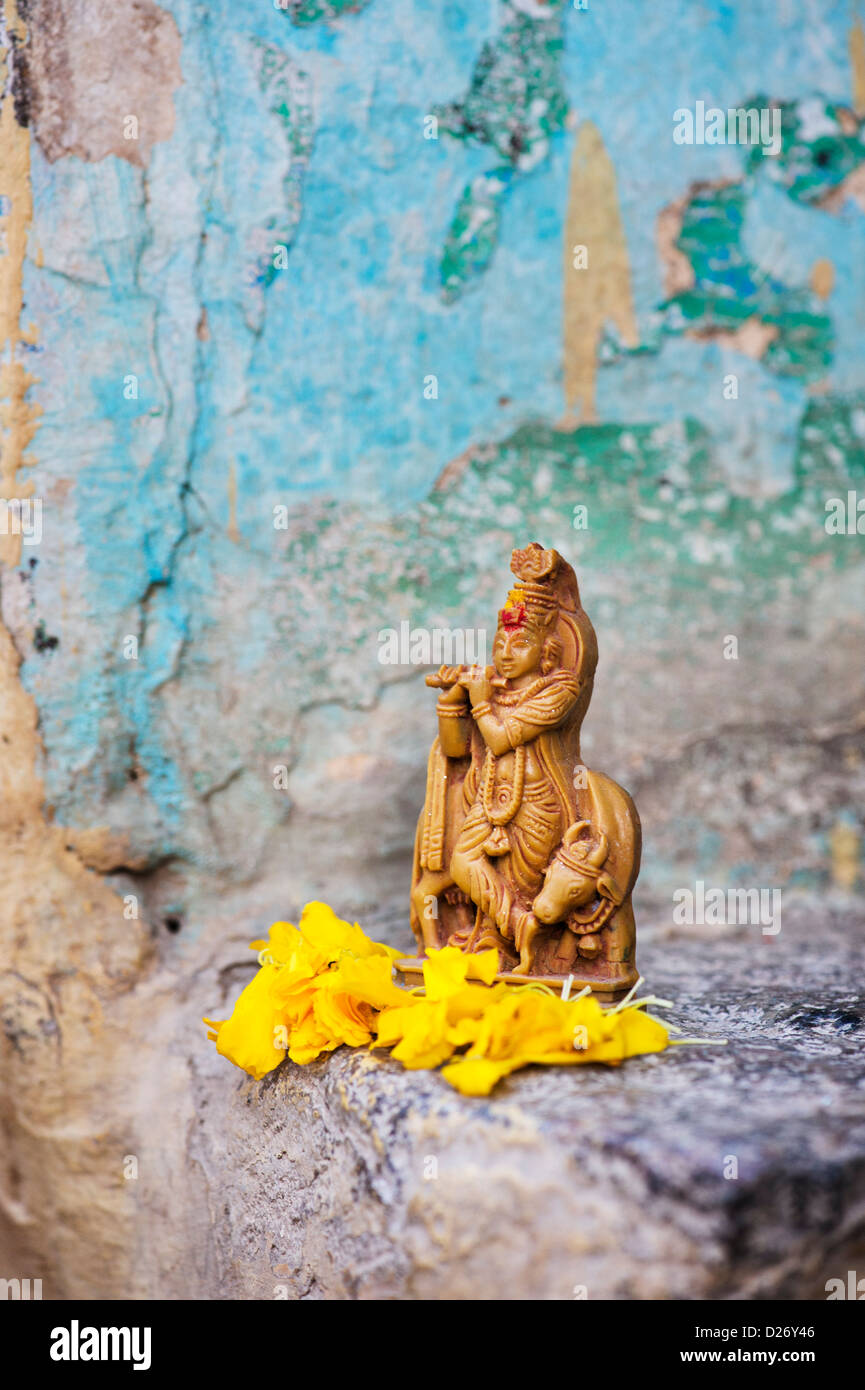 Krishna statua e petali di fiori contro la parete colorata. India Foto Stock