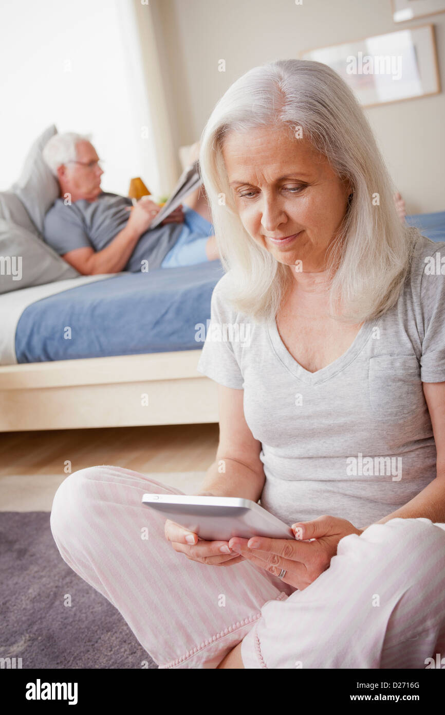 Senior donna tenendo il photo frame, uomo seduto sul letto in background Foto Stock