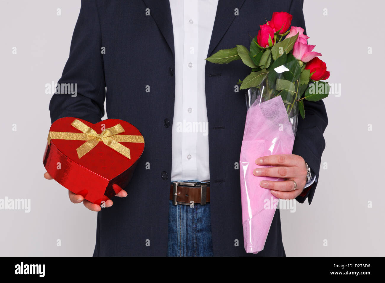 L'uomo tenendo un mazzo di fiori e una scatola di cioccolatini a forma di cuore. Foto Stock