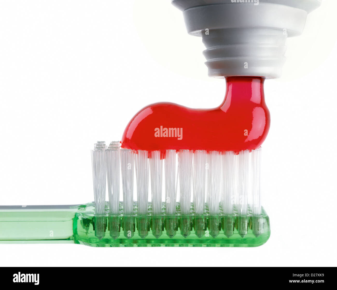 Red dentifricio essendo spremuto fuori sul Verde traslucido spazzolino da denti su sfondo bianco Foto Stock