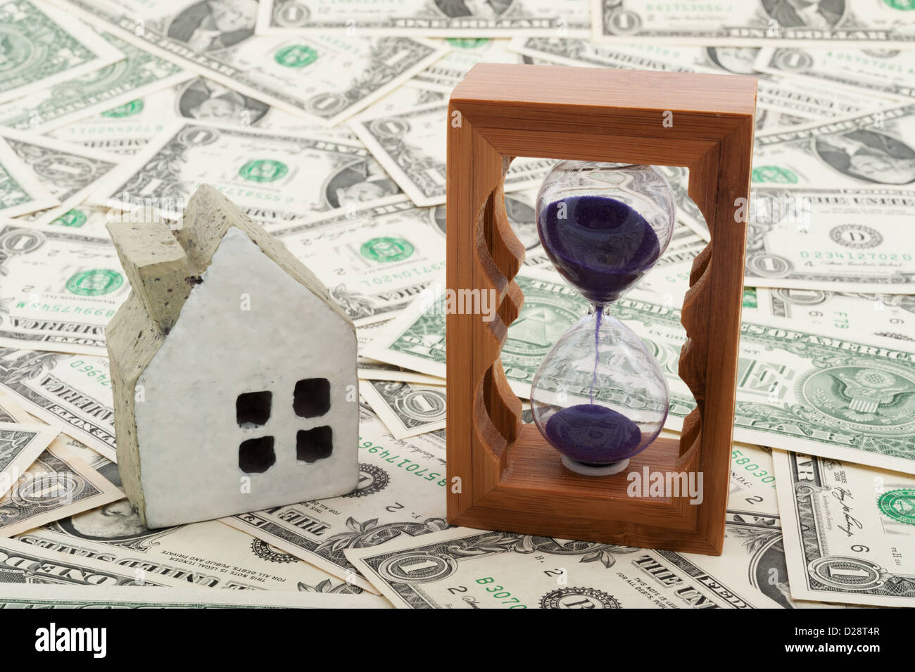 Modello di casa e clessidra su pile di carta moneta Foto Stock
