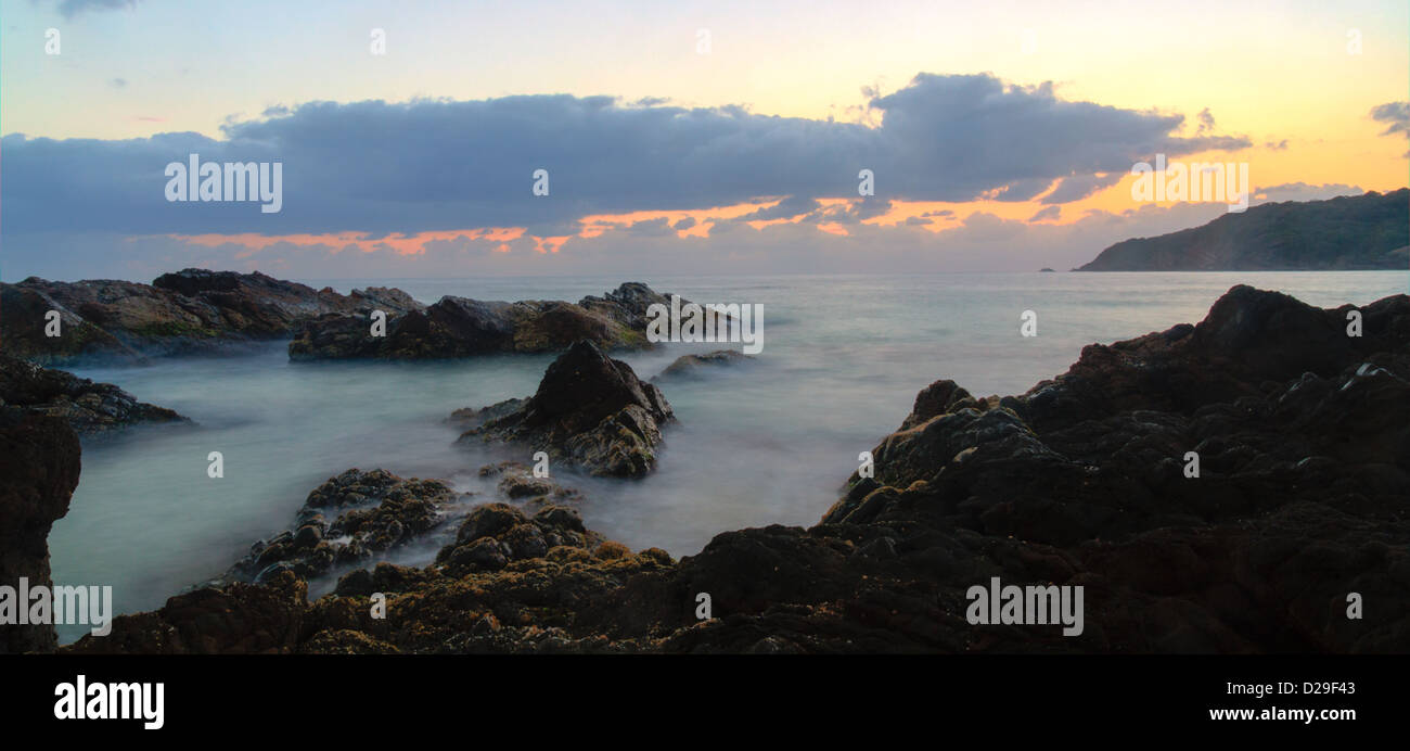 Uno Nuvoloso Tramonto in una spiaggia rocciosa Foto Stock