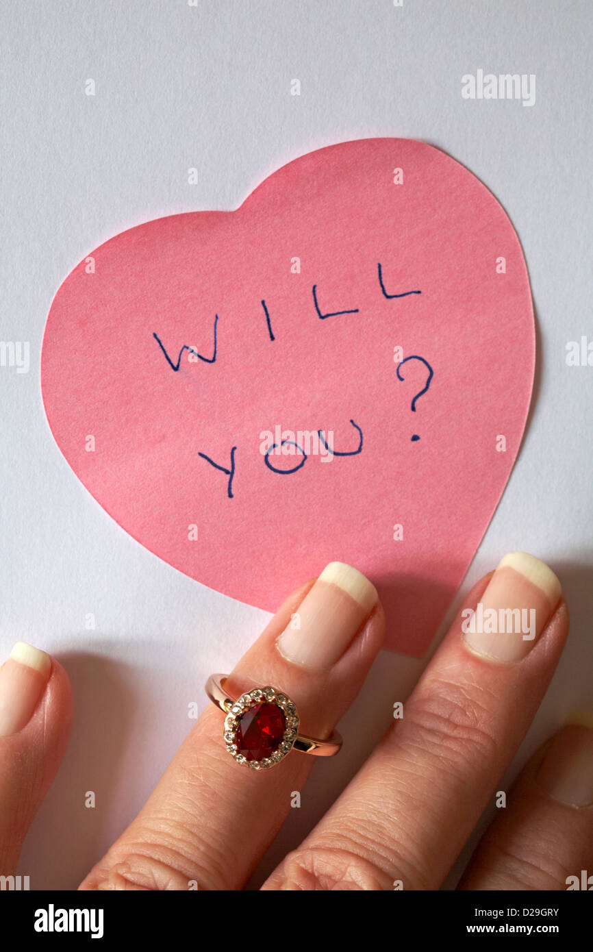 Sarà lei? Messaggio scritto sul rosa a forma di cuore post-it con le dita la messa su anello di fidanzamento - Pronto per il giorno di San Valentino o anno bisestile Foto Stock