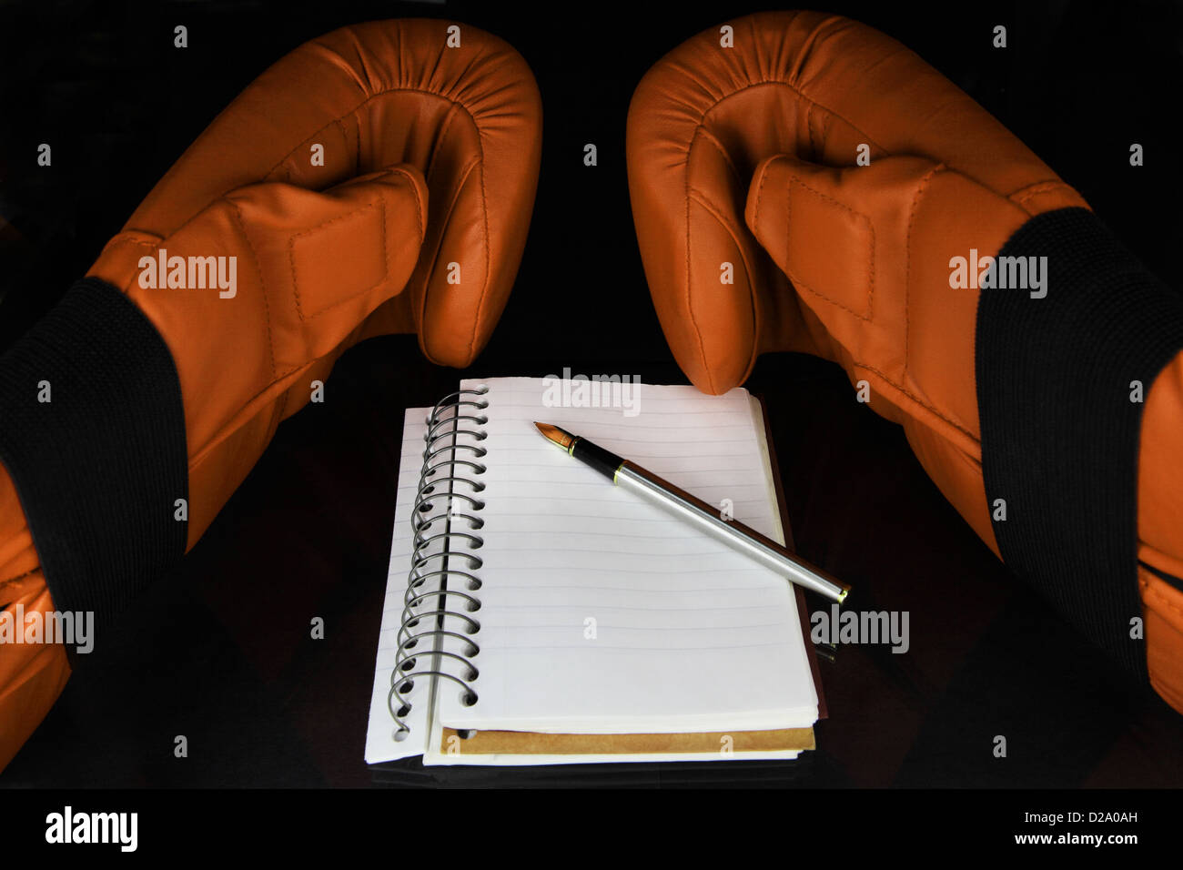 Un paio di guanti da pugilato, un notebook e una penna su una superficie scura. Foto Stock