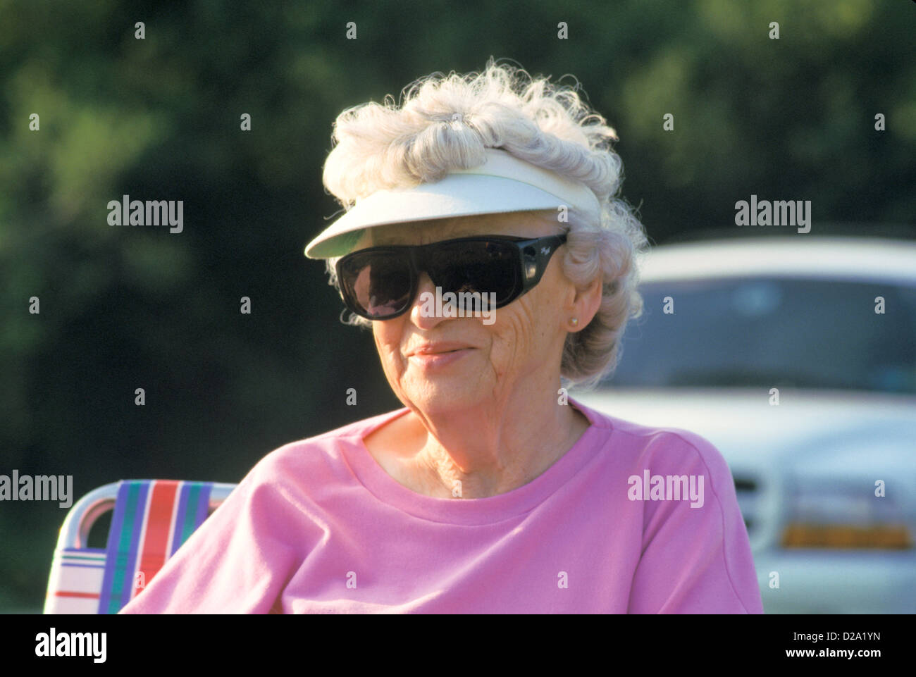 Illinois. Senior donna che indossa la visiera parasole e avvolgere gli occhiali da sole. Foto Stock